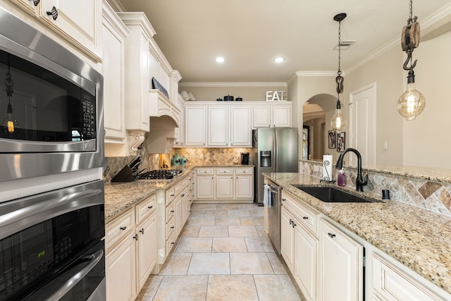 kitchen featuring stainless steel appliances, arched walkways, a sink, tasteful backsplash, and ornamental molding
