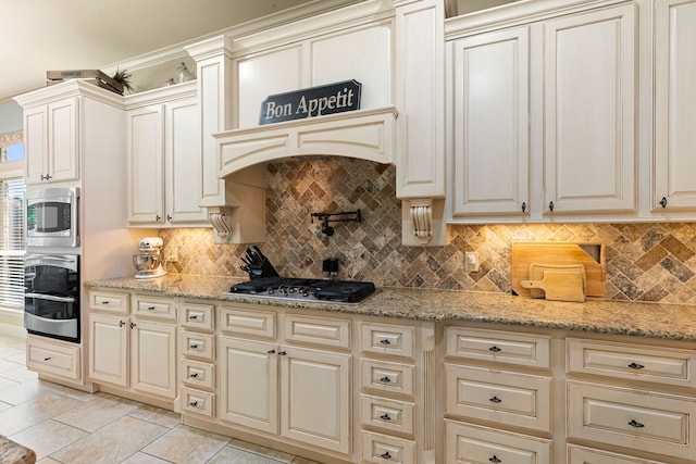 kitchen featuring light stone countertops, decorative backsplash, cream cabinetry, and appliances with stainless steel finishes