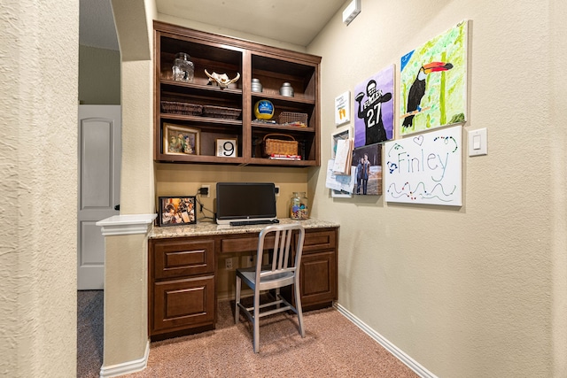office space featuring light carpet, baseboards, built in desk, and a textured wall