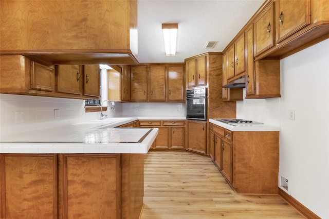 110 Dickens Landing Dr, Livingston, TX 77351 - kitchen featuring brown cabinets, a sink, black oven, light wood-type flooring, and visible vents
