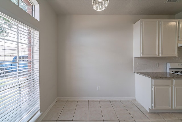 kitchen featuring white cabinets, backsplash, light stone countertops, baseboards, and a chandelier
