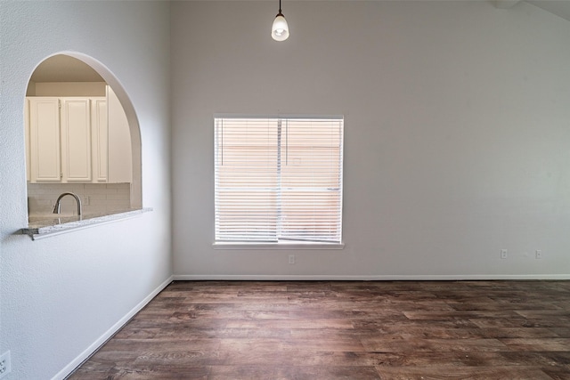 empty room featuring arched walkways, baseboards, a sink, and dark wood-style flooring