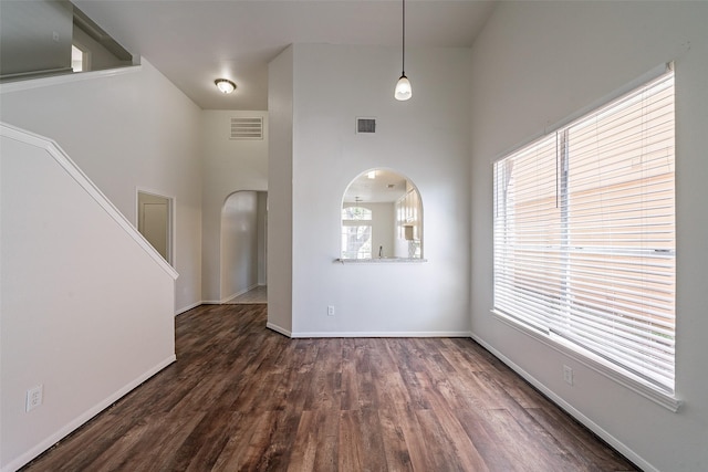 unfurnished living room with baseboards, visible vents, arched walkways, and dark wood-style flooring