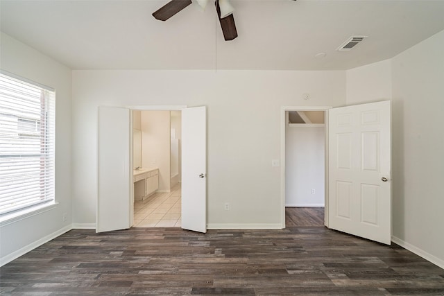 unfurnished bedroom featuring wood finished floors, connected bathroom, ceiling fan, baseboards, and visible vents