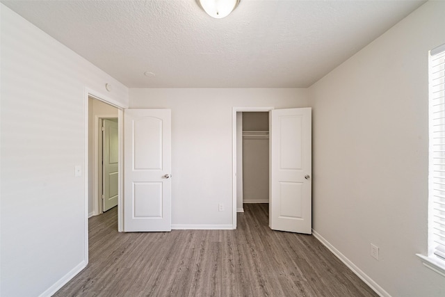unfurnished bedroom with baseboards, wood finished floors, a textured ceiling, and a closet