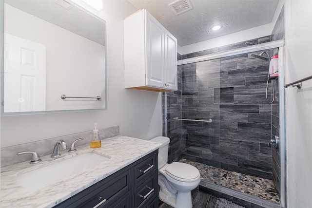 bathroom featuring a textured ceiling, a stall shower, vanity, toilet, and visible vents