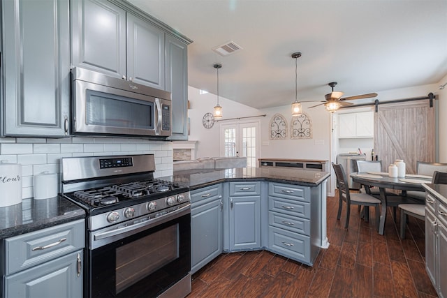 kitchen featuring a barn door, stainless steel appliances, visible vents, a peninsula, and dark wood-style flooring