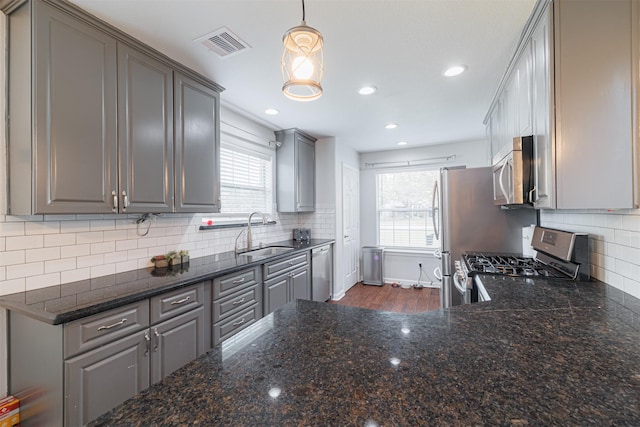 kitchen with a sink, gray cabinets, backsplash, appliances with stainless steel finishes, and visible vents
