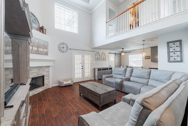 living area featuring dark wood finished floors, a towering ceiling, ornamental molding, french doors, and a fireplace