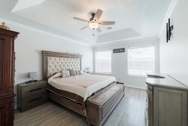 bedroom featuring wood finished floors, a textured ceiling, ceiling fan, a tray ceiling, and visible vents