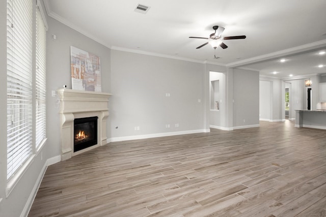 unfurnished living room with light wood finished floors, a glass covered fireplace, visible vents, a ceiling fan, and crown molding