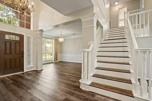 entryway with dark wood-style floors, decorative columns, a notable chandelier, stairway, and ornamental molding