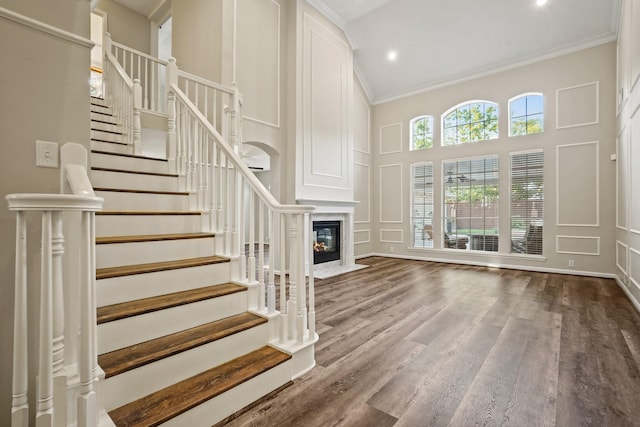 unfurnished living room featuring stairway, a decorative wall, crown molding, and a high ceiling