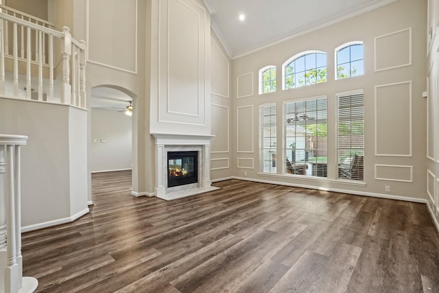 unfurnished living room with a towering ceiling, a ceiling fan, a premium fireplace, a decorative wall, and crown molding