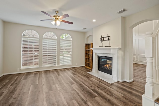 unfurnished living room featuring a ceiling fan, wood finished floors, arched walkways, a fireplace, and baseboards
