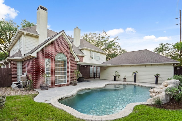 rear view of house featuring a fenced in pool, a chimney, fence, brick siding, and a patio area