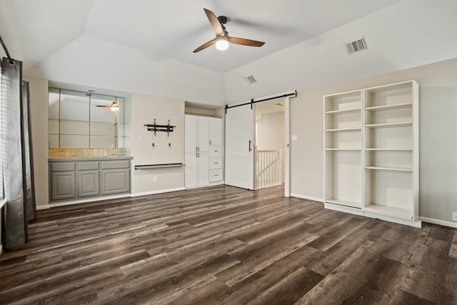 unfurnished bedroom featuring a barn door, dark wood finished floors, vaulted ceiling, and visible vents