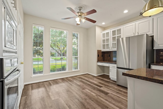 kitchen with stainless steel appliances, tasteful backsplash, baseboards, built in desk, and white cabinetry