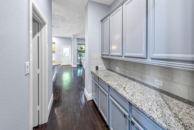 interior space featuring dark wood-type flooring, a textured ceiling, baseboards, and decorative columns