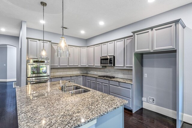 kitchen with dark wood-style flooring, a sink, arched walkways, baseboards, and appliances with stainless steel finishes