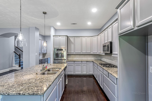 kitchen featuring stainless steel appliances, visible vents, a sink, dark wood-type flooring, and a center island with sink