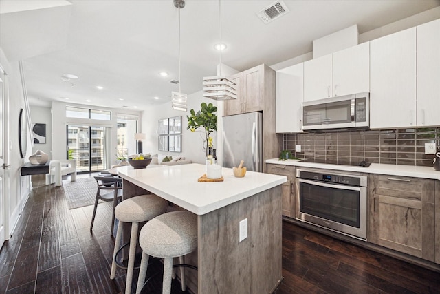 kitchen featuring a kitchen bar, dark wood finished floors, appliances with stainless steel finishes, and visible vents