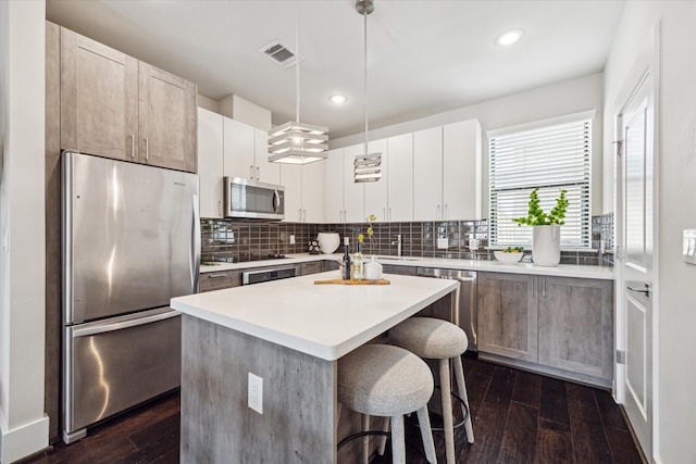 kitchen featuring a kitchen breakfast bar, tasteful backsplash, dark wood finished floors, visible vents, and appliances with stainless steel finishes