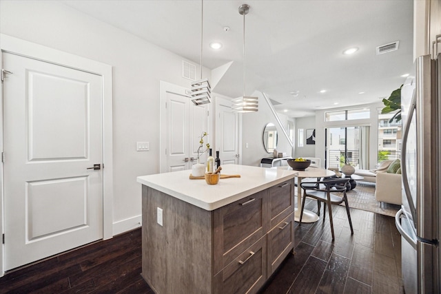 kitchen with light countertops, visible vents, dark wood-type flooring, freestanding refrigerator, and a center island