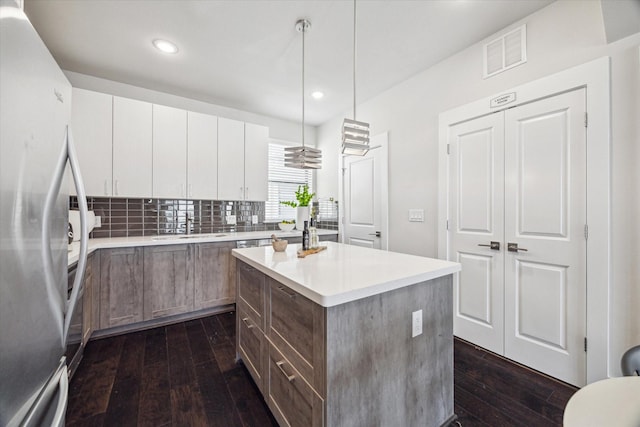 kitchen with freestanding refrigerator, backsplash, dark wood-style flooring, visible vents, and a kitchen island