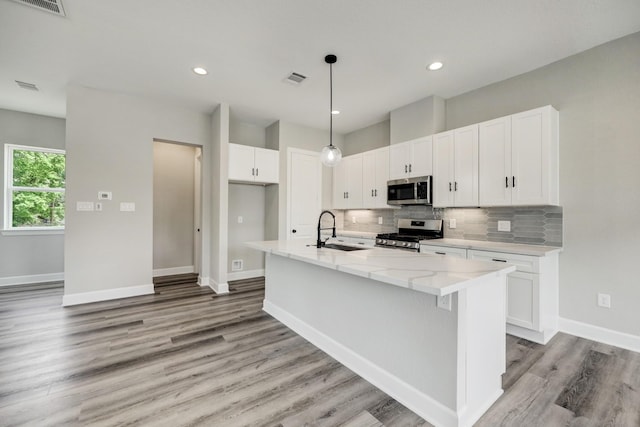 kitchen with a sink, decorative backsplash, light wood finished floors, appliances with stainless steel finishes, and visible vents