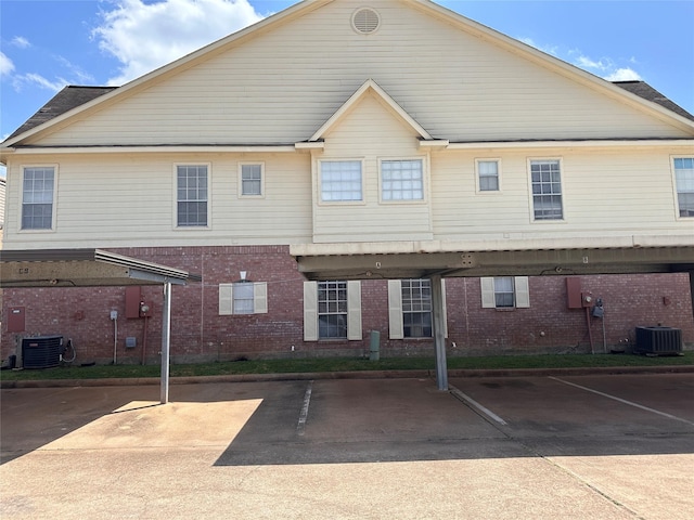 back of house featuring central AC unit, brick siding, and covered parking