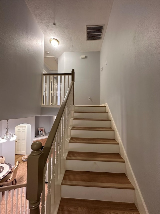 stairs with arched walkways, a textured ceiling, wood finished floors, and visible vents
