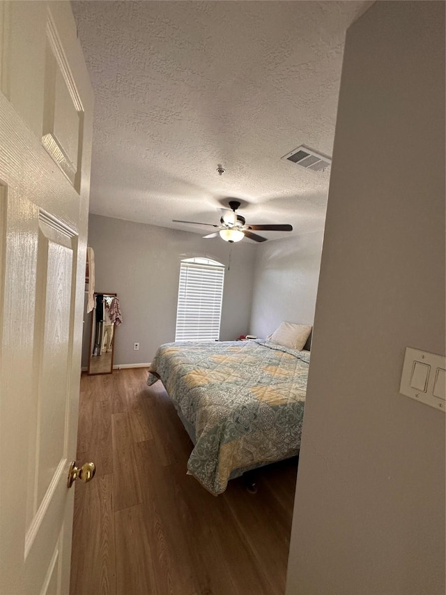 bedroom with a textured ceiling, wood finished floors, visible vents, and a ceiling fan