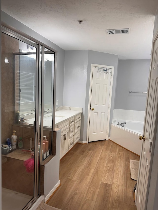 bathroom featuring a bath, a stall shower, visible vents, wood finished floors, and vanity