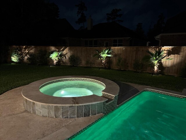 pool at night featuring an in-ground hot tub