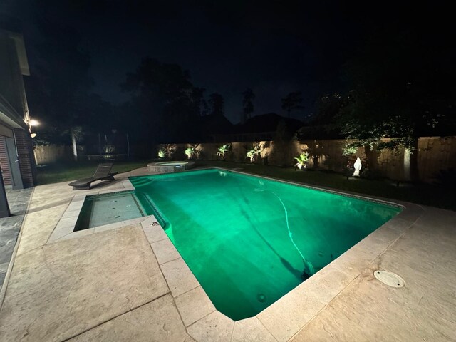 pool at twilight featuring a patio, a pool with connected hot tub, and a fenced backyard