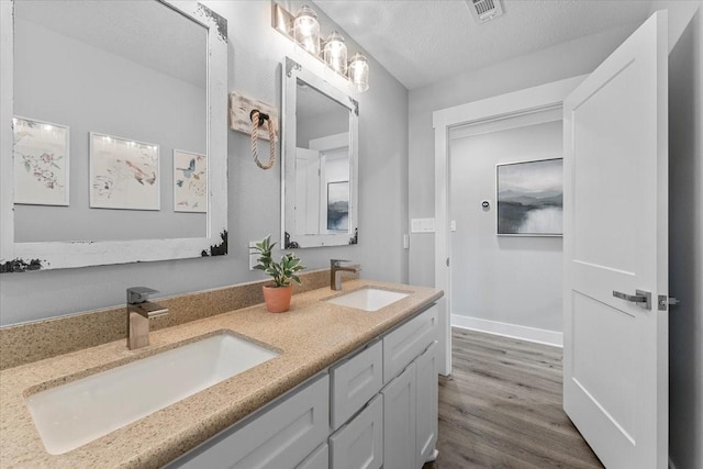 full bath featuring wood finished floors, a sink, visible vents, and double vanity