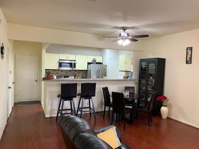 interior space featuring a ceiling fan, decorative backsplash, a breakfast bar, stainless steel appliances, and dark wood-type flooring