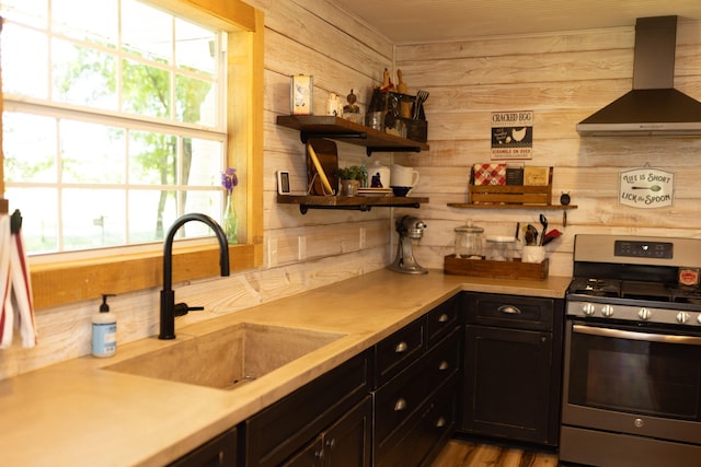 1867 Fm 2423, Grapeland, TX 75844 - kitchen featuring light countertops, wooden walls, stainless steel range with gas stovetop, a sink, and wall chimney exhaust hood