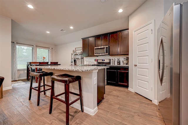 kitchen featuring appliances with stainless steel finishes, a breakfast bar, visible vents, a center island with sink, and backsplash