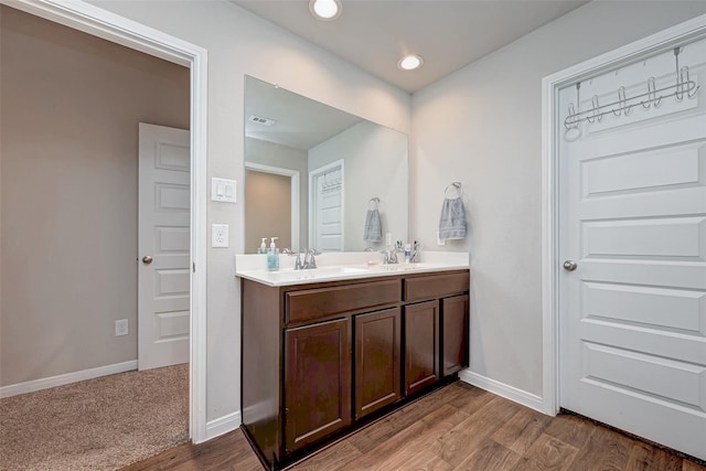 bathroom featuring a sink, double vanity, visible vents, baseboards, and wood finished floors