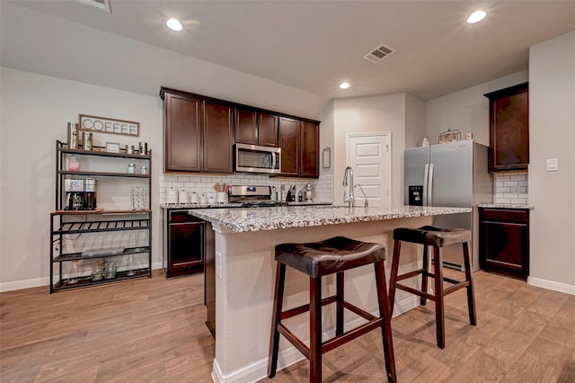 kitchen with appliances with stainless steel finishes, decorative backsplash, light wood-style flooring, and baseboards