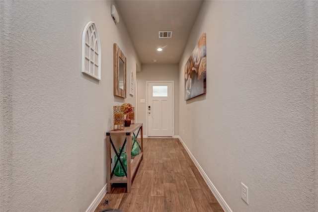 hall featuring wood finished floors, visible vents, a textured wall, and baseboards