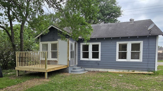 back of house featuring a lawn, roof with shingles, and a deck