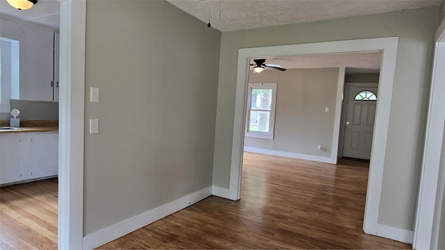 hallway featuring wood finished floors, a textured ceiling, and baseboards