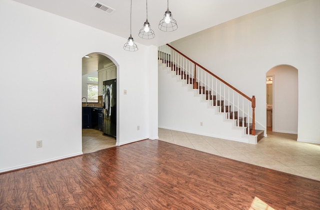 unfurnished living room featuring light wood-style flooring, arched walkways, a sink, visible vents, and stairway