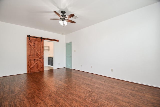 empty room with a barn door, baseboards, visible vents, a ceiling fan, and dark wood-type flooring