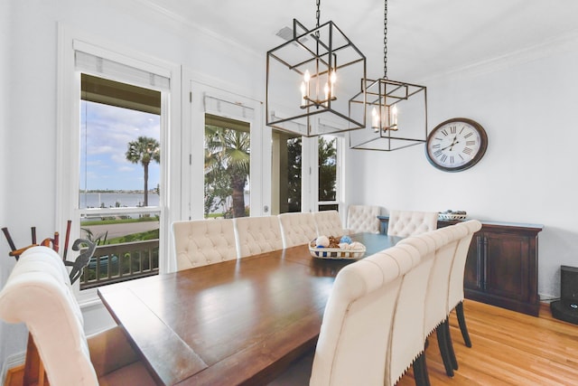dining area featuring ornamental molding, a chandelier, a water view, and light wood-style floors