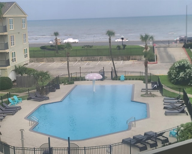 community pool with a patio, a water view, and fence