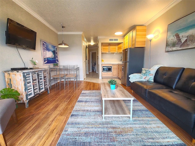 living area with crown molding, a textured ceiling, visible vents, and light wood-type flooring